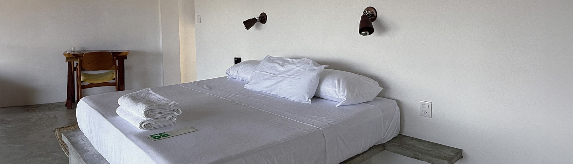 Minimalist king bed at Hotel Lalo Zipolite with concrete platform, crisp white linens, and relaxed coastal design.